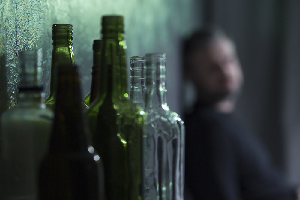 Empty alcohol bottle with a recovering alcoholic in the background