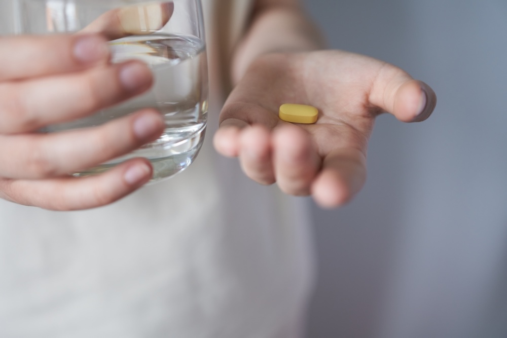 Closeup of a hand holding a yellow alprazolam pill and a glass of water